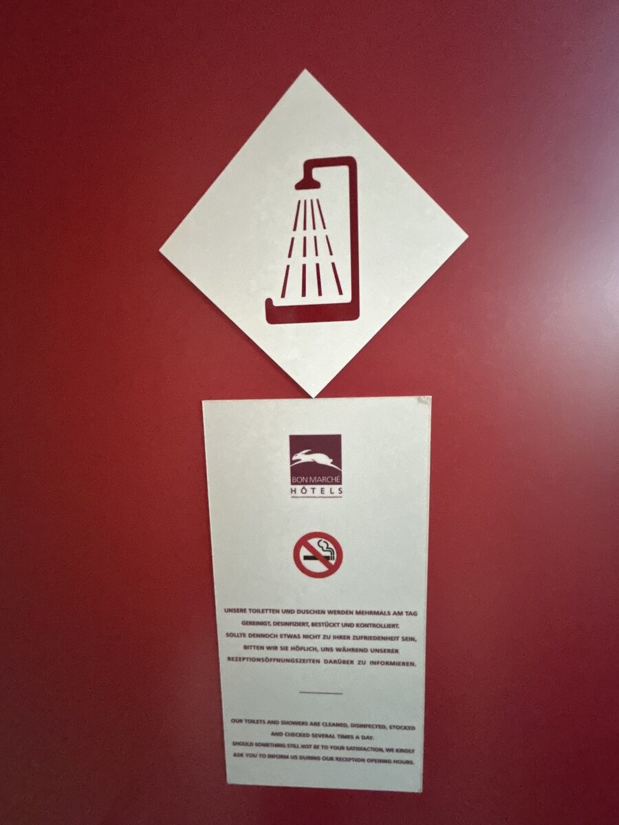 Ein stilisiertes Duschsymbol auf rotem Hintergrund mit Hinweisschild darunter