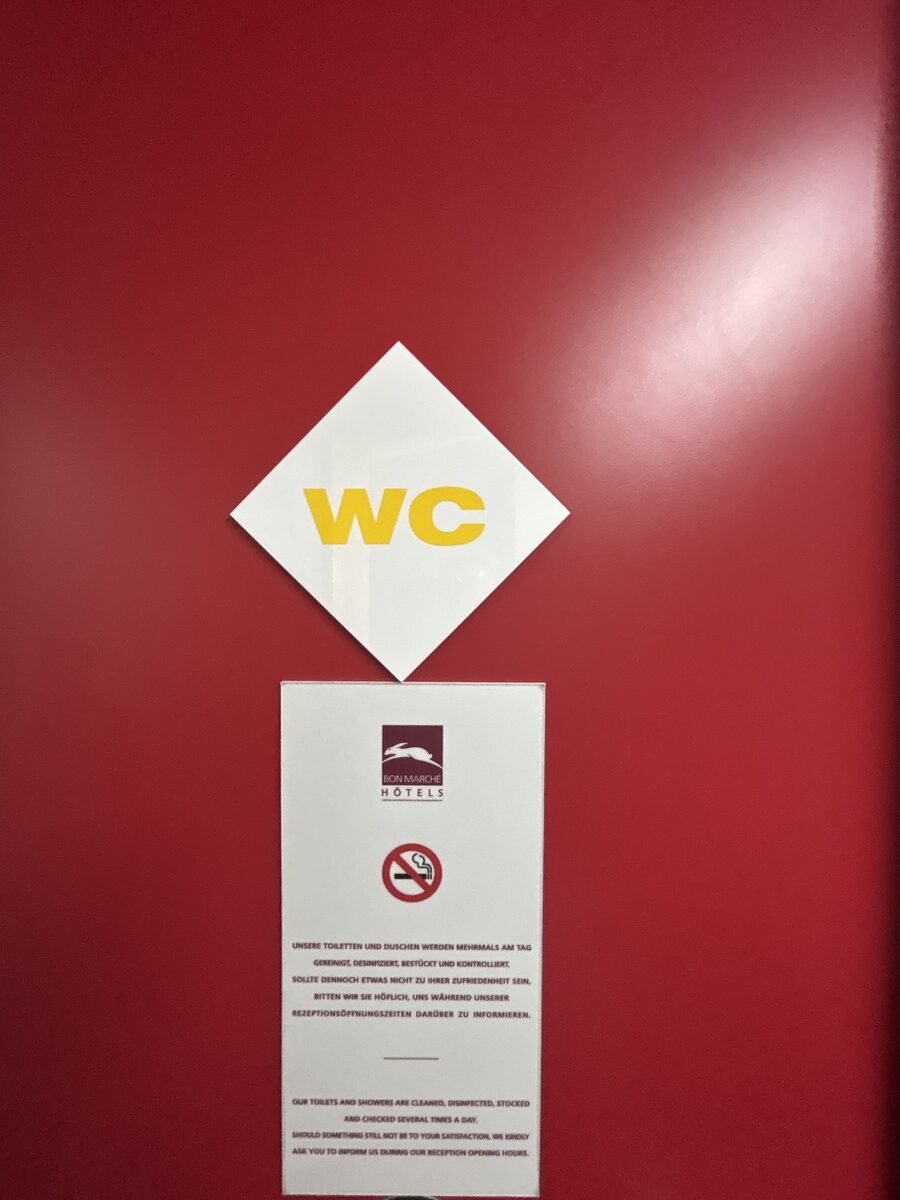 Rote Tür mit gelbem WC-Zeichen und weißem Hinweisschild darunter