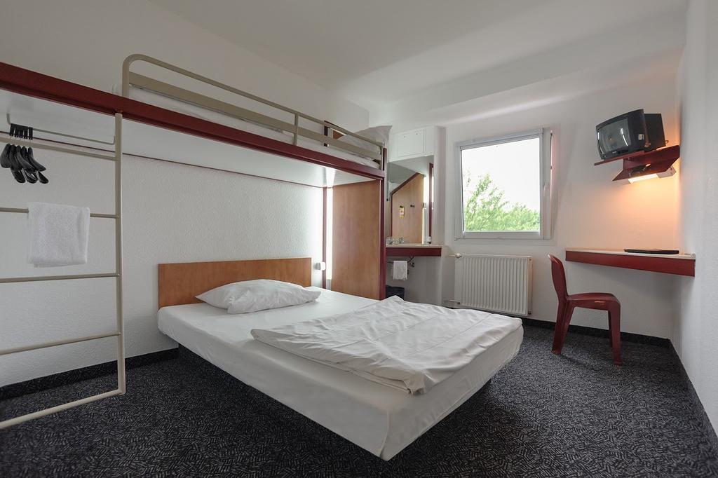 Ein schlichtes Einzelzimmer mit weißem Bett, rotem Hochbett und grauem Teppich
