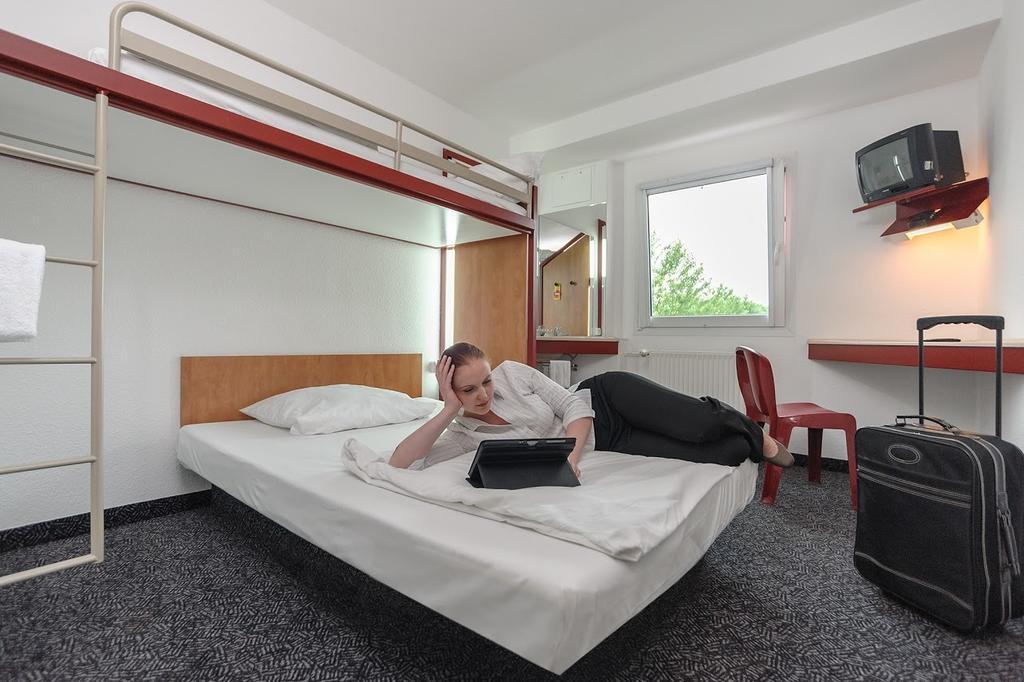 Eine Person entspannt lächelnd auf einem weißen Bett in einem schlichten Hotelzimmer