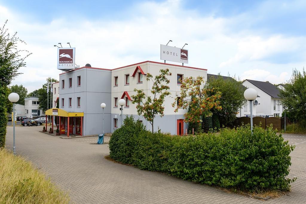 Ein modernes Hotel in Grautönen mit roten Fensterrahmen und gepflegten Büschen