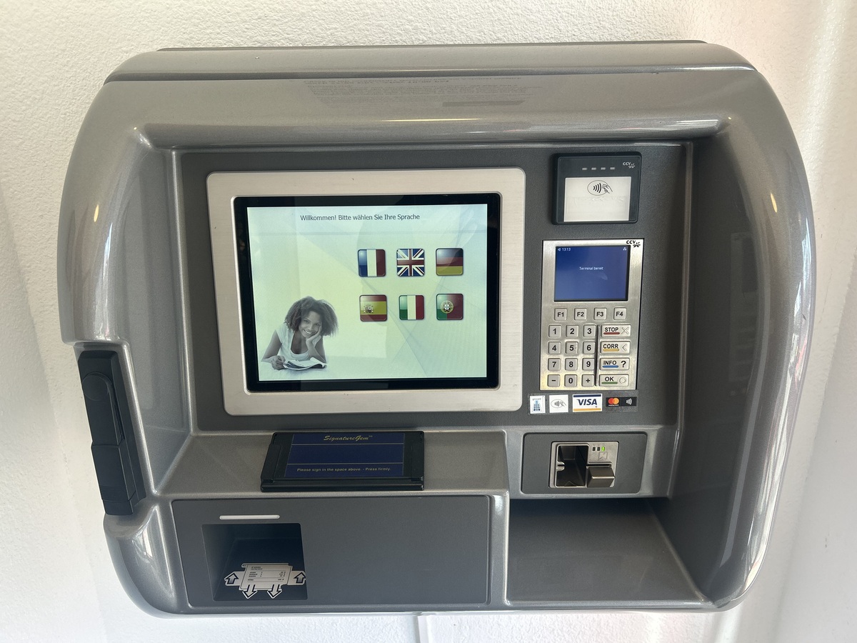 Ein grauer Bankautomat mit einem farbigen Touchscreen zeigt Sprachoptionen und Kartenschlitz