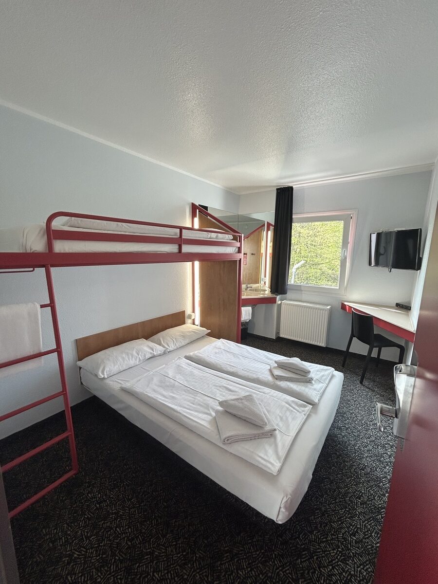 Ein Zimmer mit roten Etagenbetten, weißer Bettwäsche und einem Fenster mit Blick ins Grüne