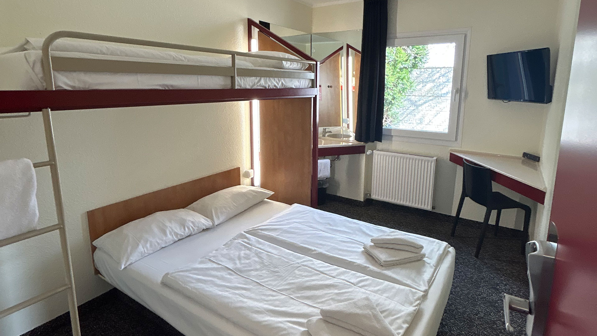 Helles Zimmer mit Doppelbett und Hochbett, weiße Bettwäsche, rotes Holz
